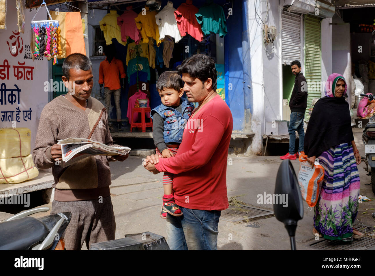 Two men and a child talking as life goes on around on a street corner. Udaipur, also known as the City of Lakes, The Venice of the East, is the historic capital of the kingdom of Mewar, Rajasthan. Stock Photo