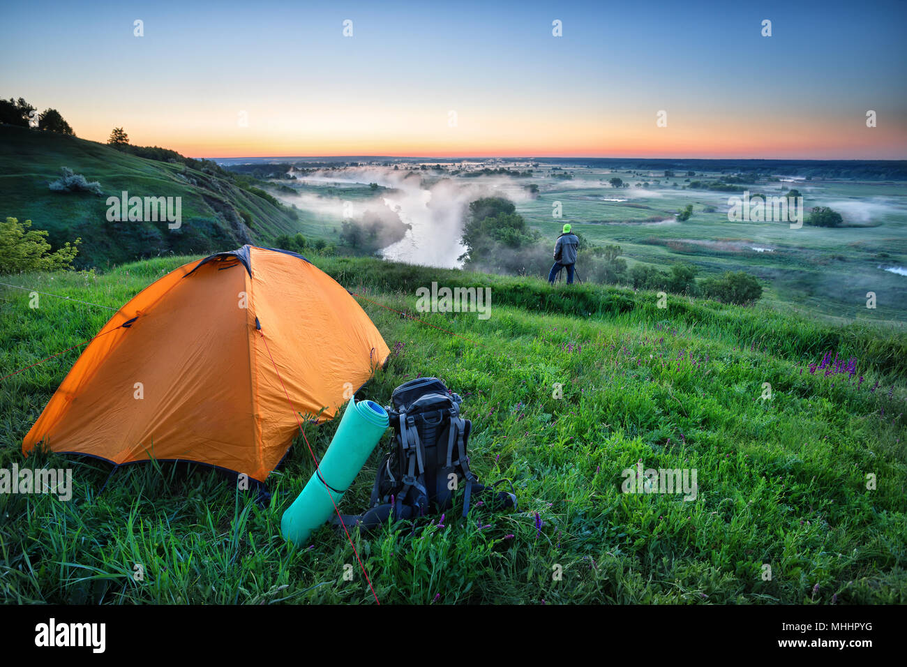 Orange tent and backpack on hill with tourist Stock Photo