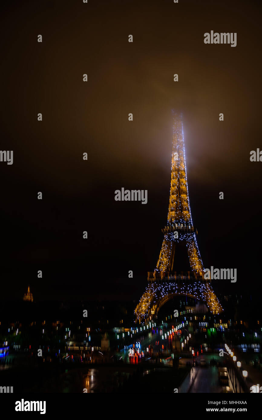 The Eiffel Tower at night with its summit in the fog / mist / clouds Stock Photo