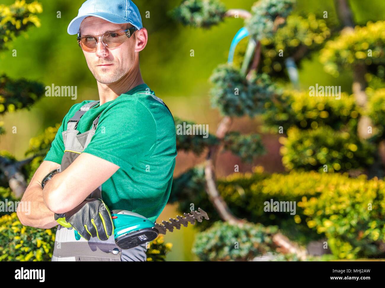 Professional Caucasian Gardener Portrait. Garden Worker with Compact Cordless Plants Trimmer. Stock Photo