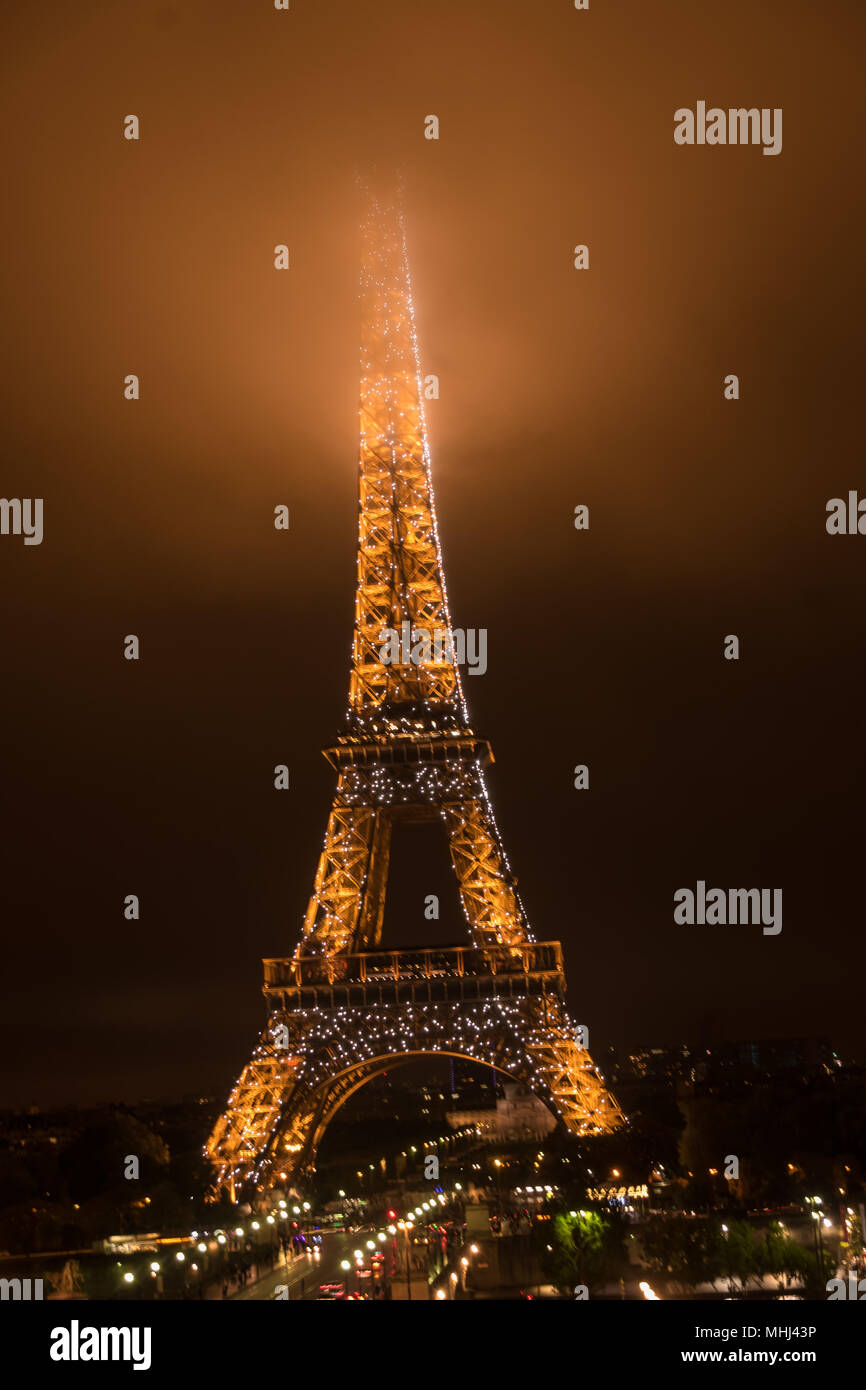 The Eiffel Tower at night with its summit in the fog / mist / clouds Stock Photo