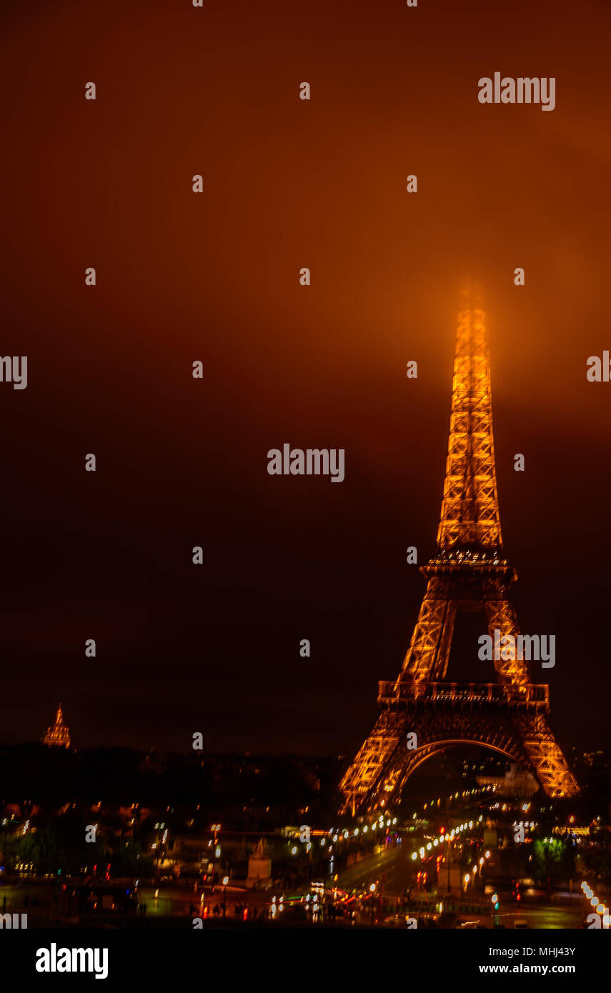 The Eiffel Tower at night with its summit in the fog / mist / clouds Stock Photo