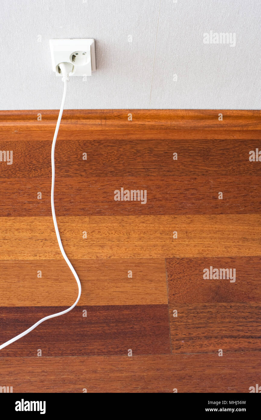Parquet Floor And Electric Plug Connected To The Outlet In A Wall
