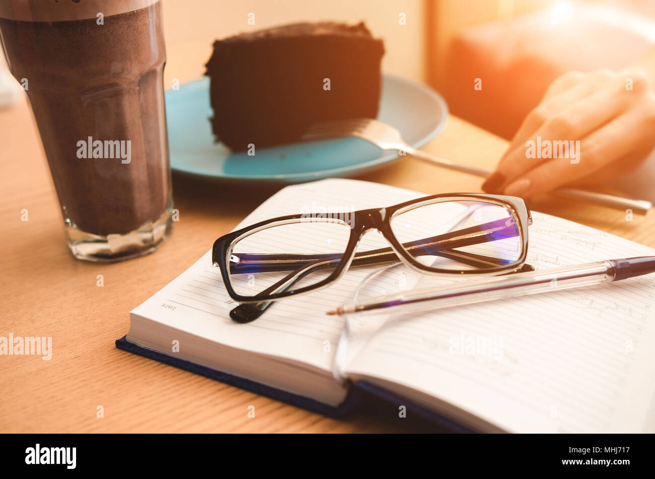 Still life: Eyeglasses and pen on open notebook.  Coffee cup and piece of cake. Fork in hand. Planning concept Stock Photo