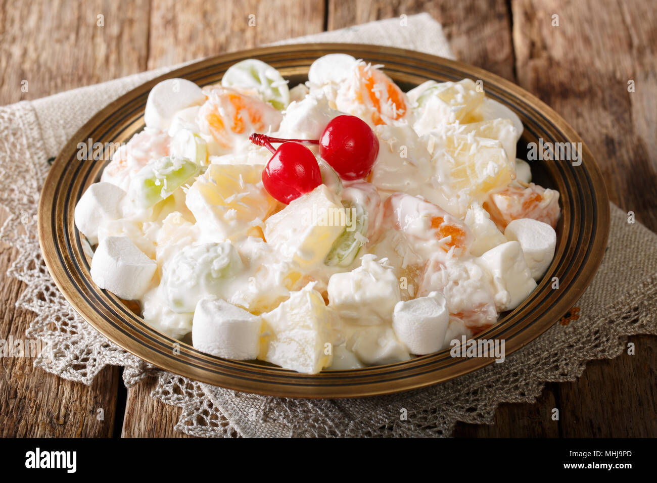 fruit salad from pineapple, oranges, grapes and coconut with marshmallow and vanilla yogurt close-up on a plate. horizontal Stock Photo