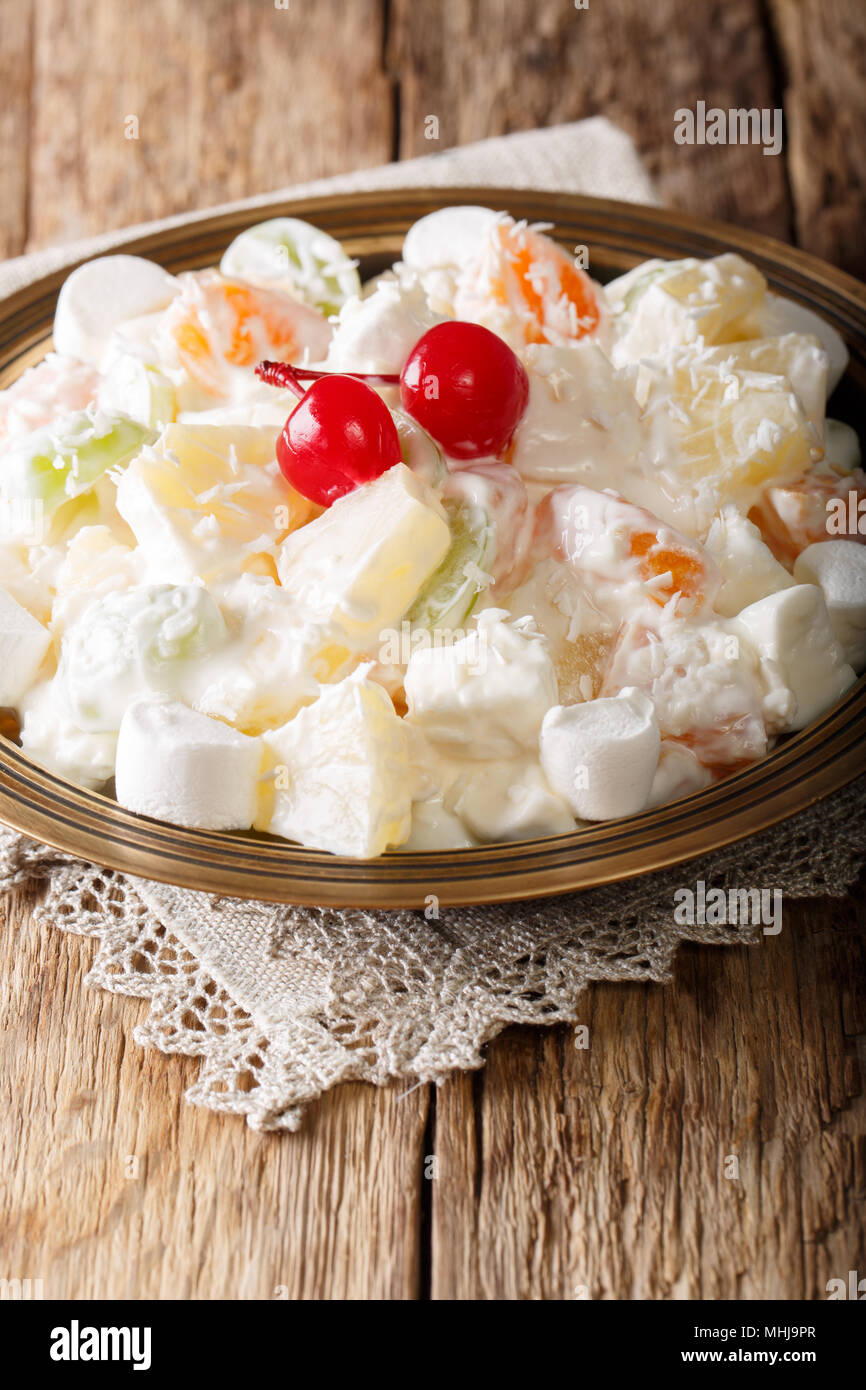Delicious sweet fruit salad Ambrosia made from pineapple, tangerine, grapes and marshmelow with vanilla yogurt close-up on a plate. vertical Stock Photo