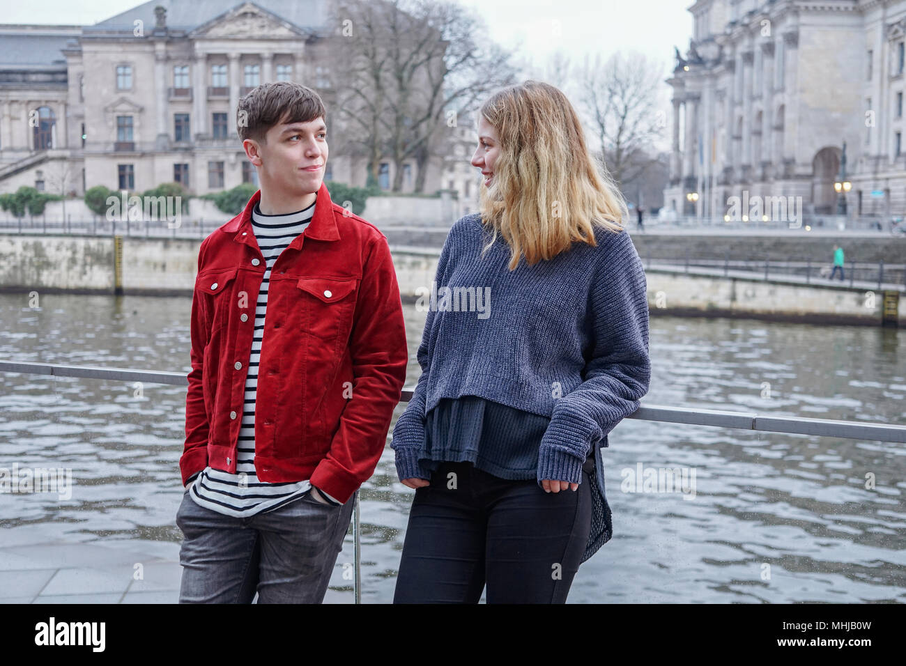 young woman and man hanging out by the river Spree in Berlin, Germany, with Bundestag Reichstag building in the background Stock Photo