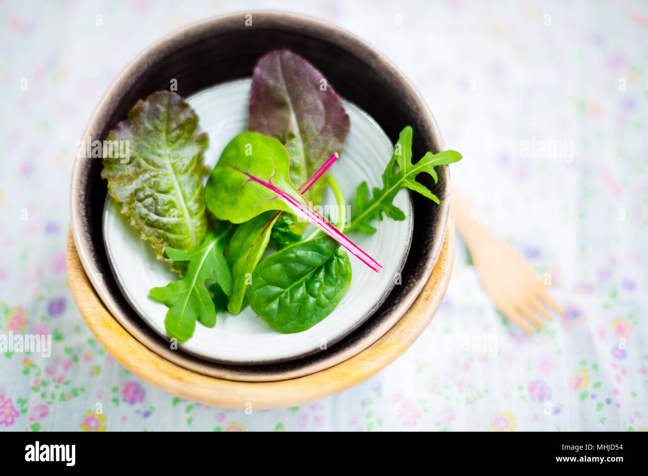 Mixed baby leaf salad of red chard, arugula, red lettuce and tatsoi in small bowls on a floral napkin, Selective focus Stock Photo