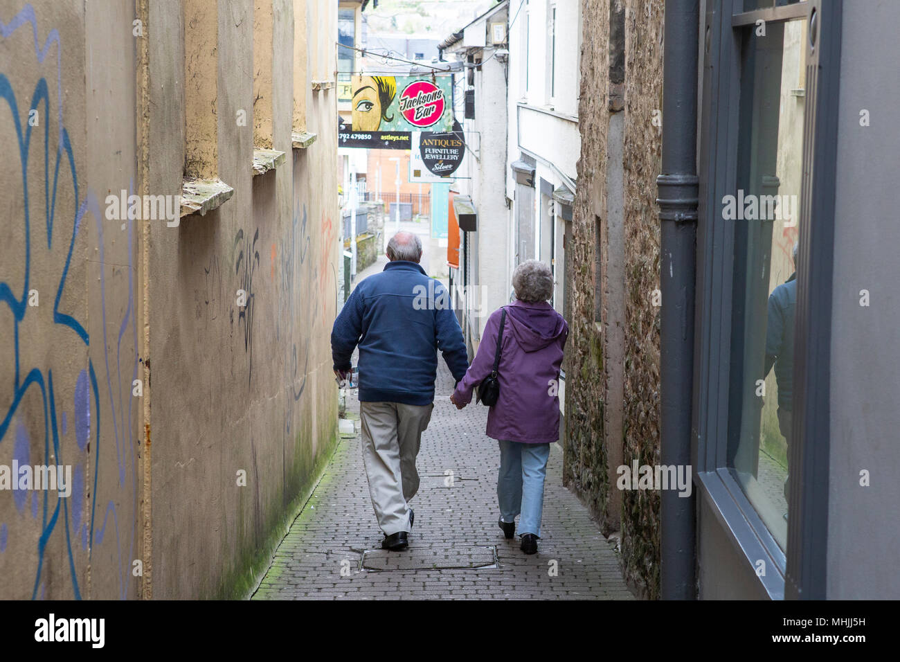 Elderly /senior couple walk hand in hand through narrow street in town Stock Photo