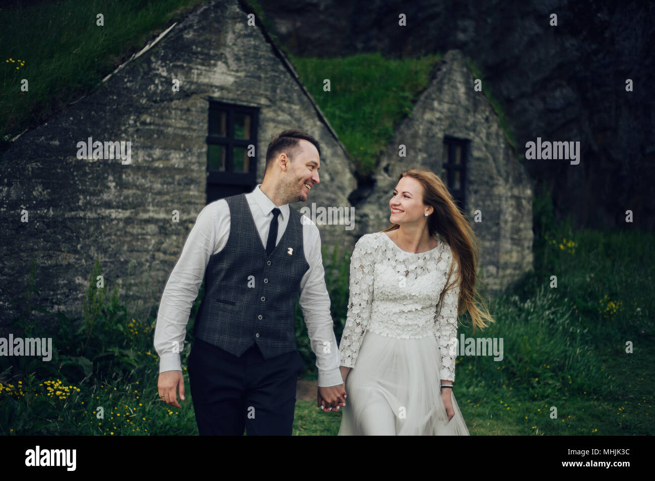 Young stylish fashion couple in love in Iceland. Woman and man embrace and want to kiss each other. Stone mountains and Icelandic house on the background. Stock Photo