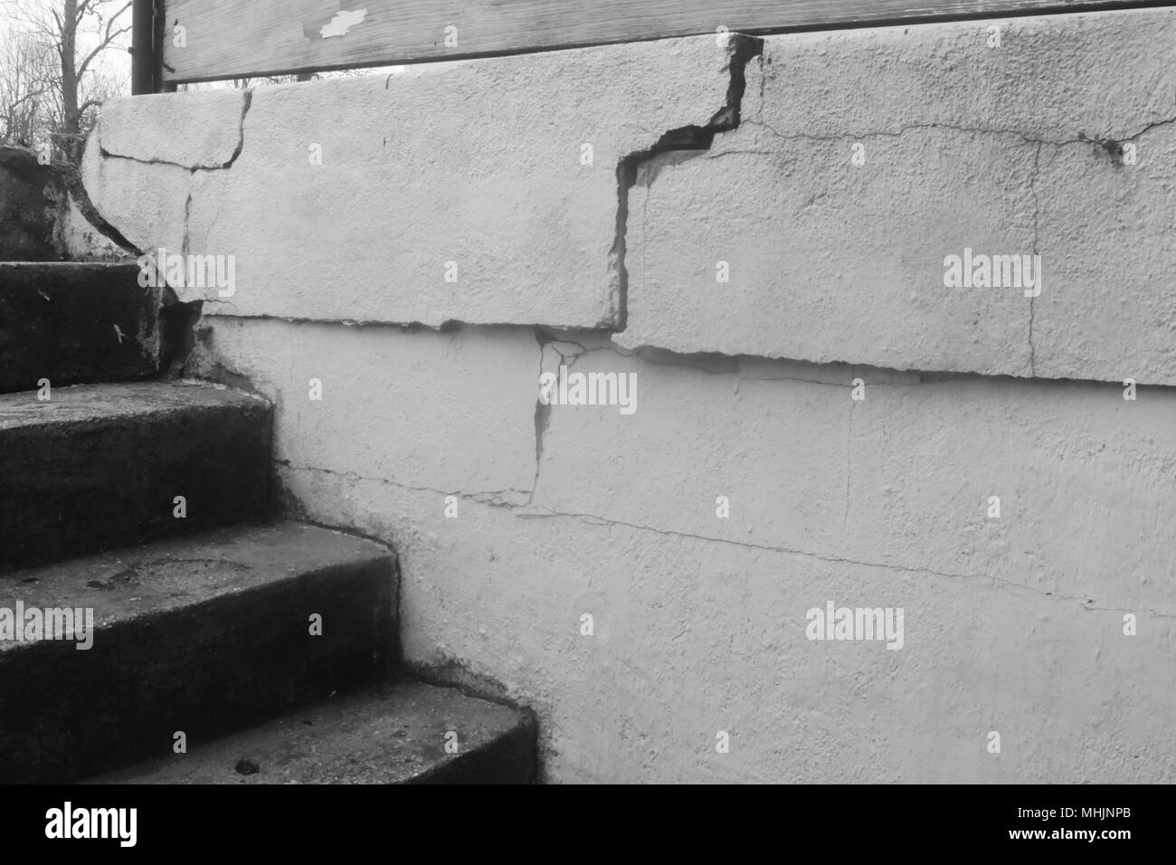 Black and white photo of old concrete stairs leading to a basement, and a cracked retaining wall. Rural Missouri, MO, United States, US, USA. Stock Photo