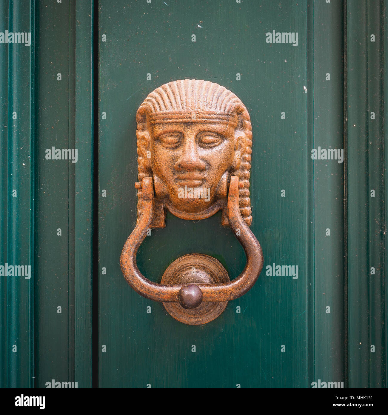 Brass door knocker representing an ancient Egyptian head on a dark green wooden door. Squared format. Stock Photo