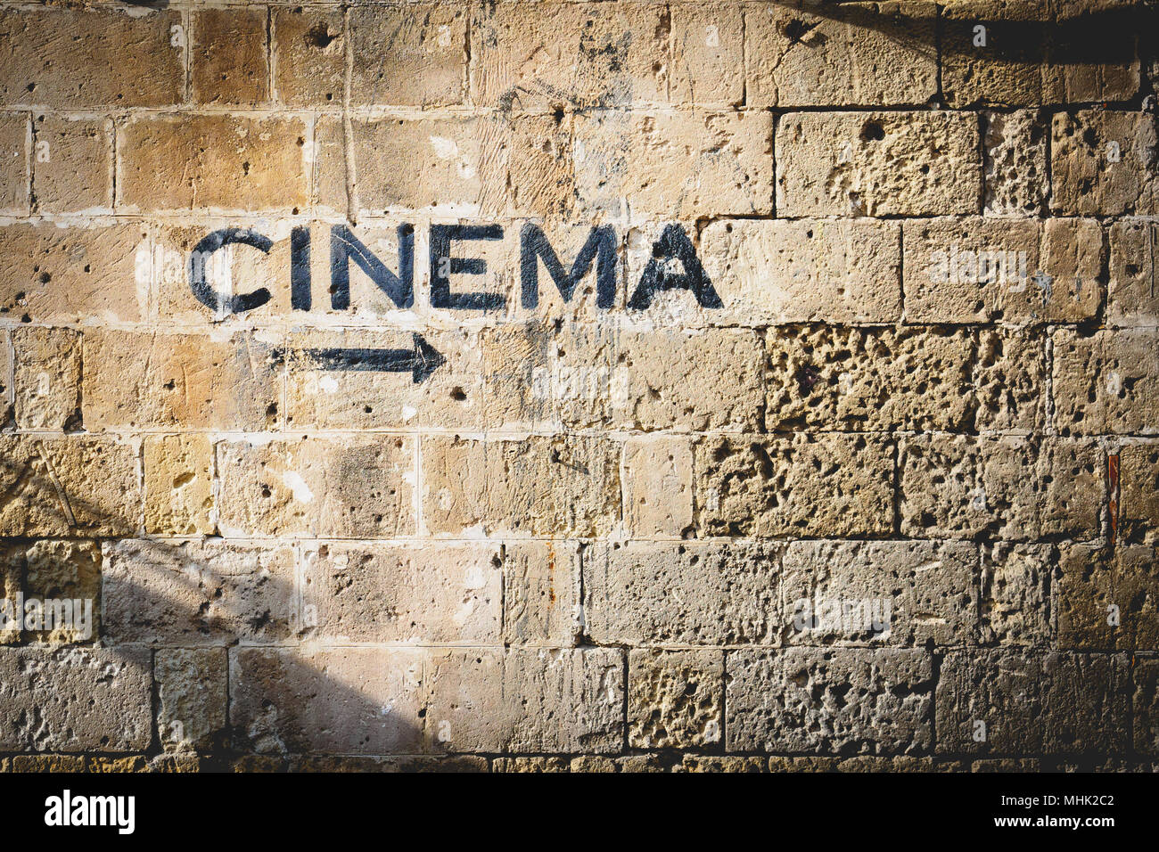 The word 'cinema' and an arrow pointing the right side painted in black on a stone wall. Landscape format. Stock Photo