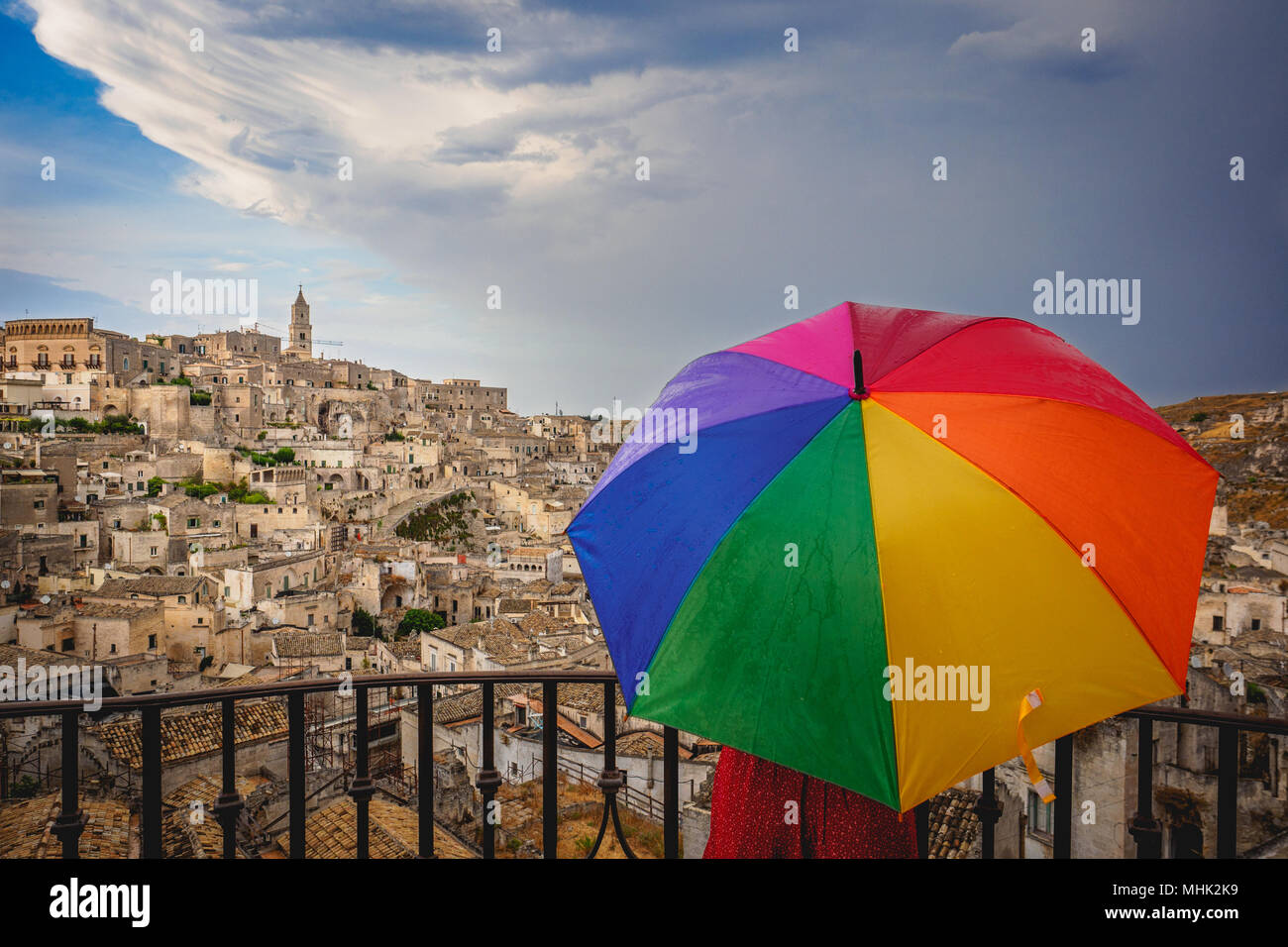 Matera (Italy), September 2017. Tourist with a rainbow umbrella at the belvedere over the ancient town called 'Sassi di Matera'. Landscape format. Stock Photo