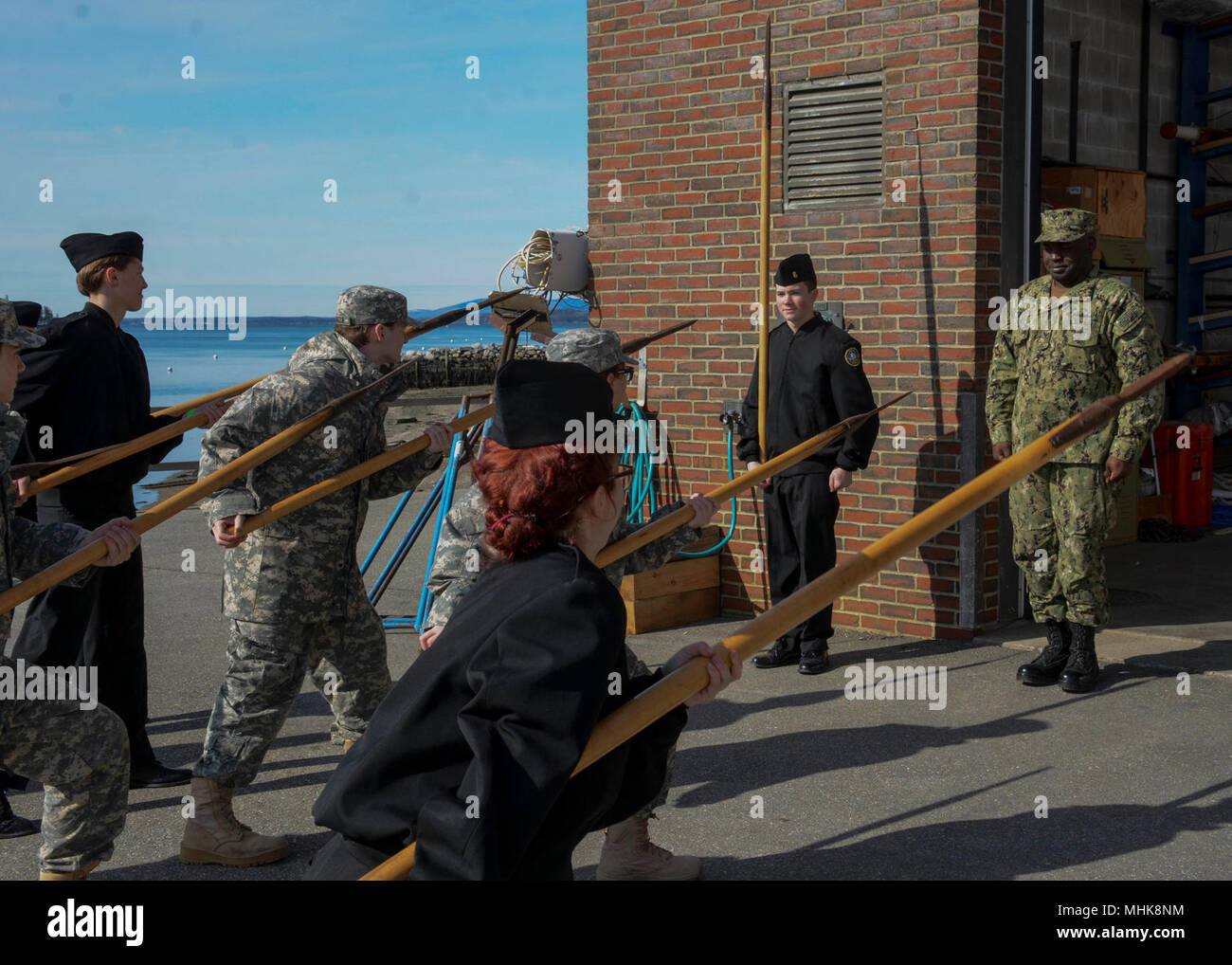 (March 24, 2018) Ship’s Serviceman 2nd Class Jeremy Lusk, assigned to USS Constitution, observes as JROTC cadets perform pike drills at Marine Maritime Academy. Constitution Sailors visited Maine Maritime Academy to teach JROTC cadets teamwork and history through gun and pike drills. (U.S. Navy Stock Photo