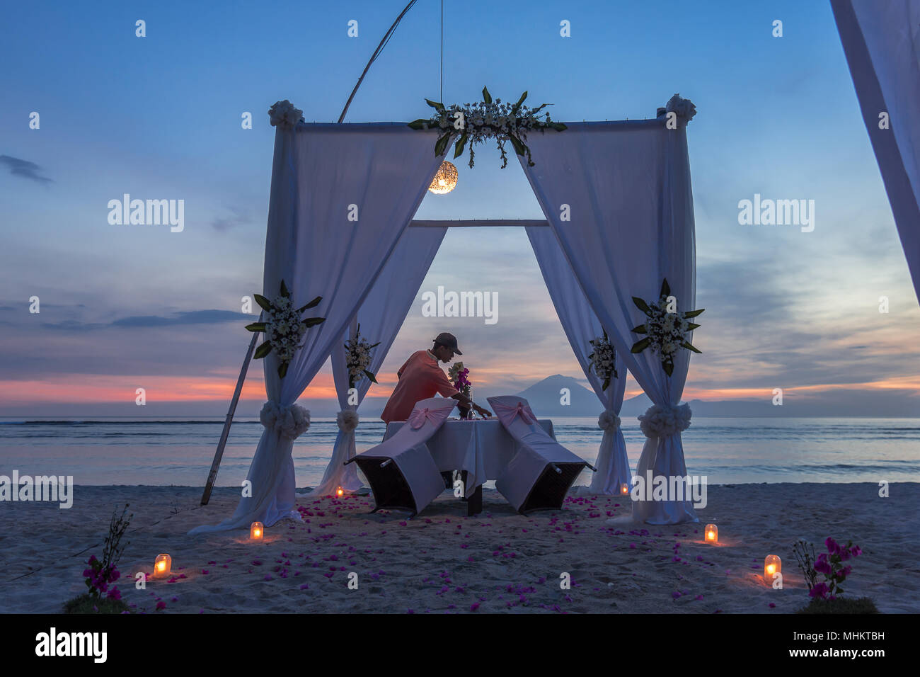 A seafront romantic dinner in the sunset during the blue hour is prepared by a boy in a cap, april 24, 2018, Gili Trawangan, Indonesia Stock Photo