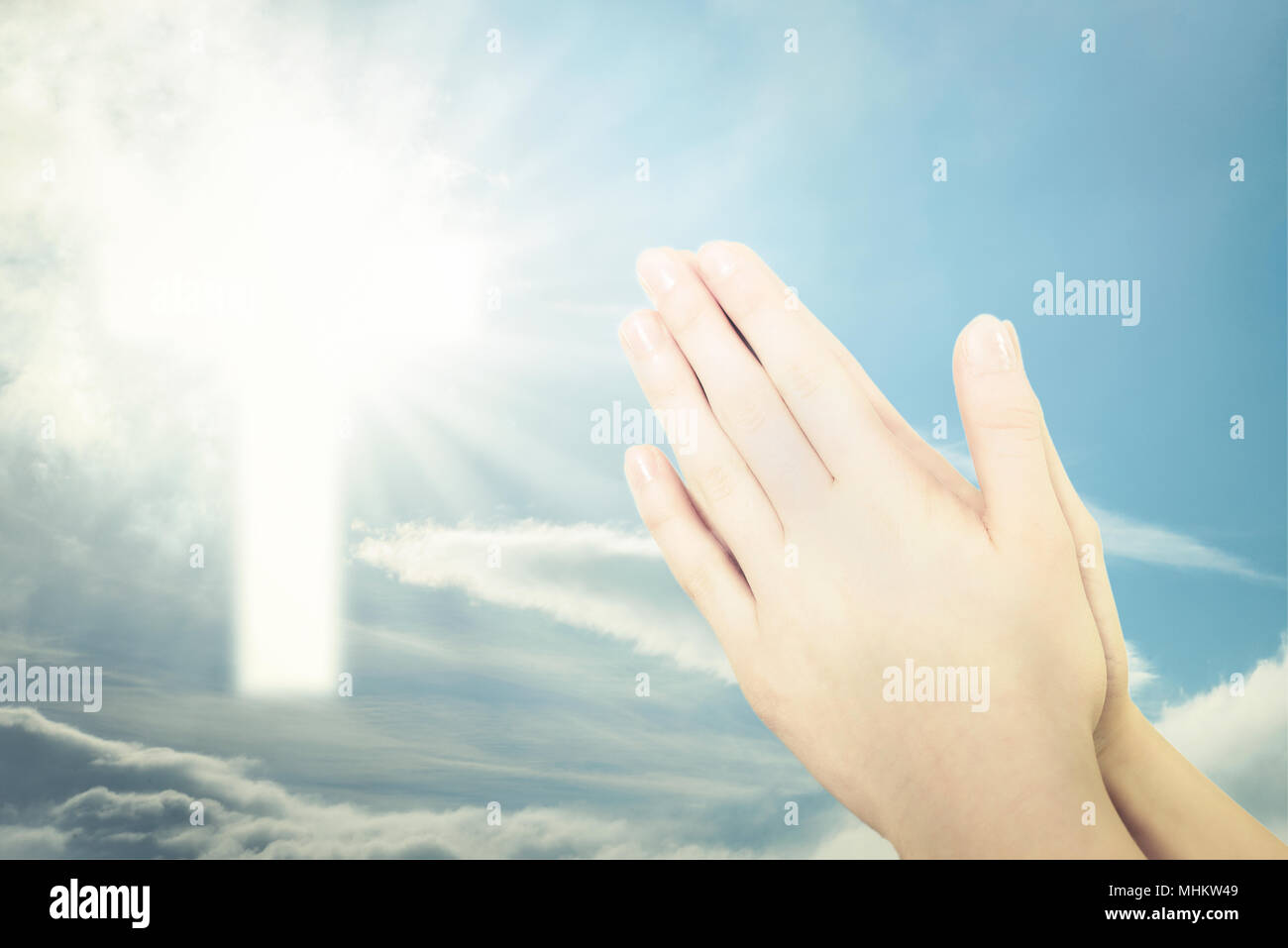 Concept of Christian prayer - folded hands for prayer against a blue sky and a shining cross sign (mixed) Stock Photo