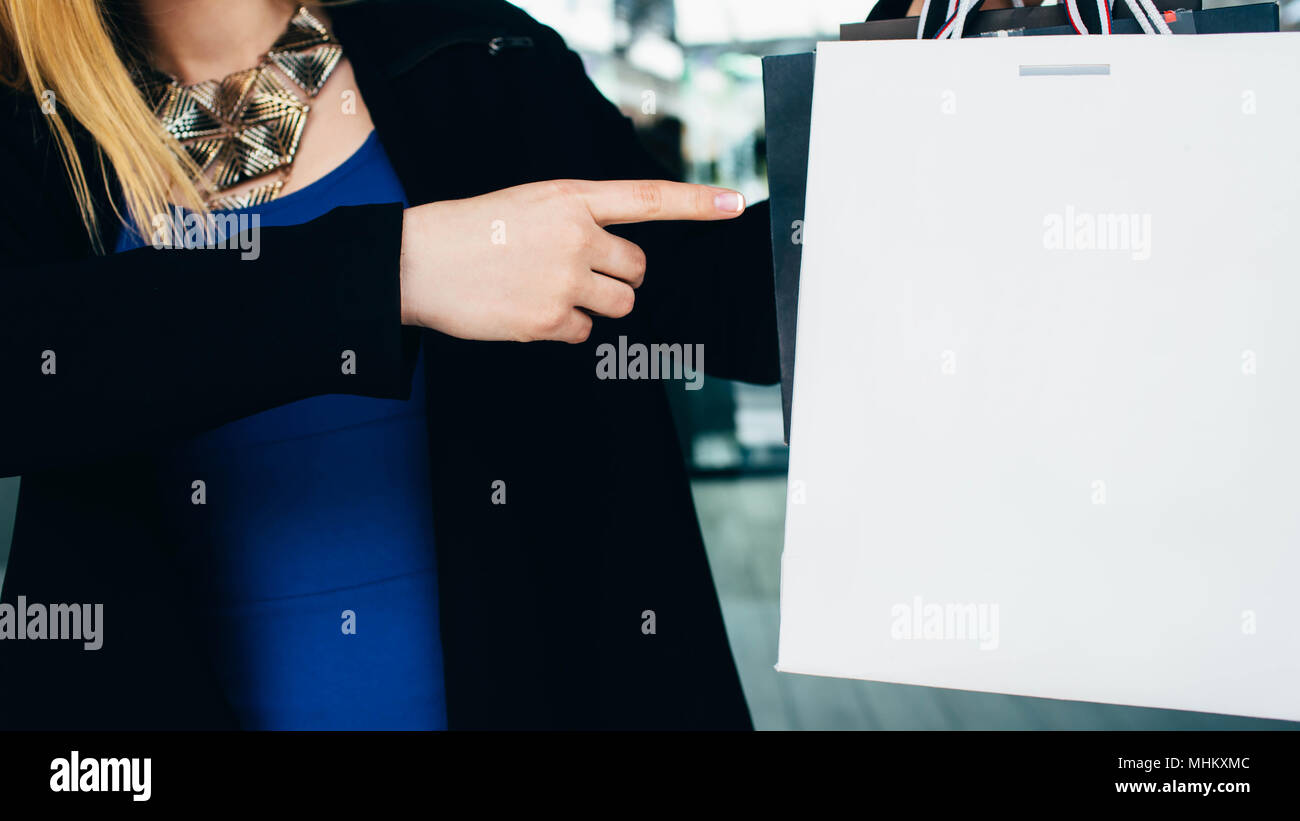 woman points with her finger at the shopping bag, with empty space. White shopping package, purchase concept Stock Photo