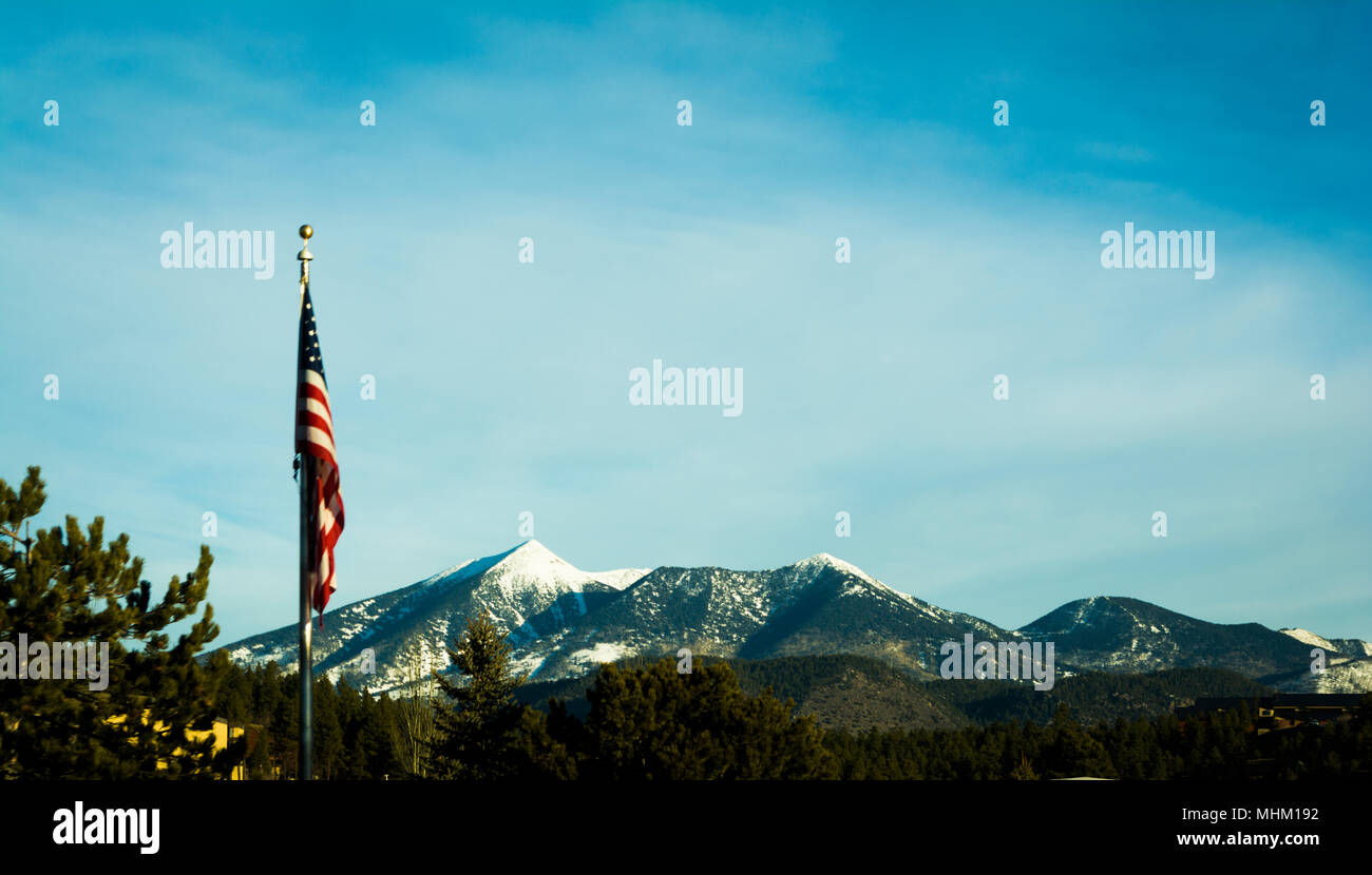 American Flag flying in a blue sky with snowy mountain peaks in the