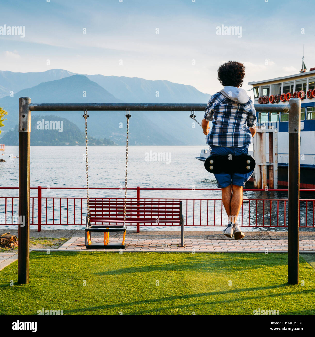 Unidentifiable teenager plays on a swing overlooking Lake Como, Lombardy, Italy. Stock Photo