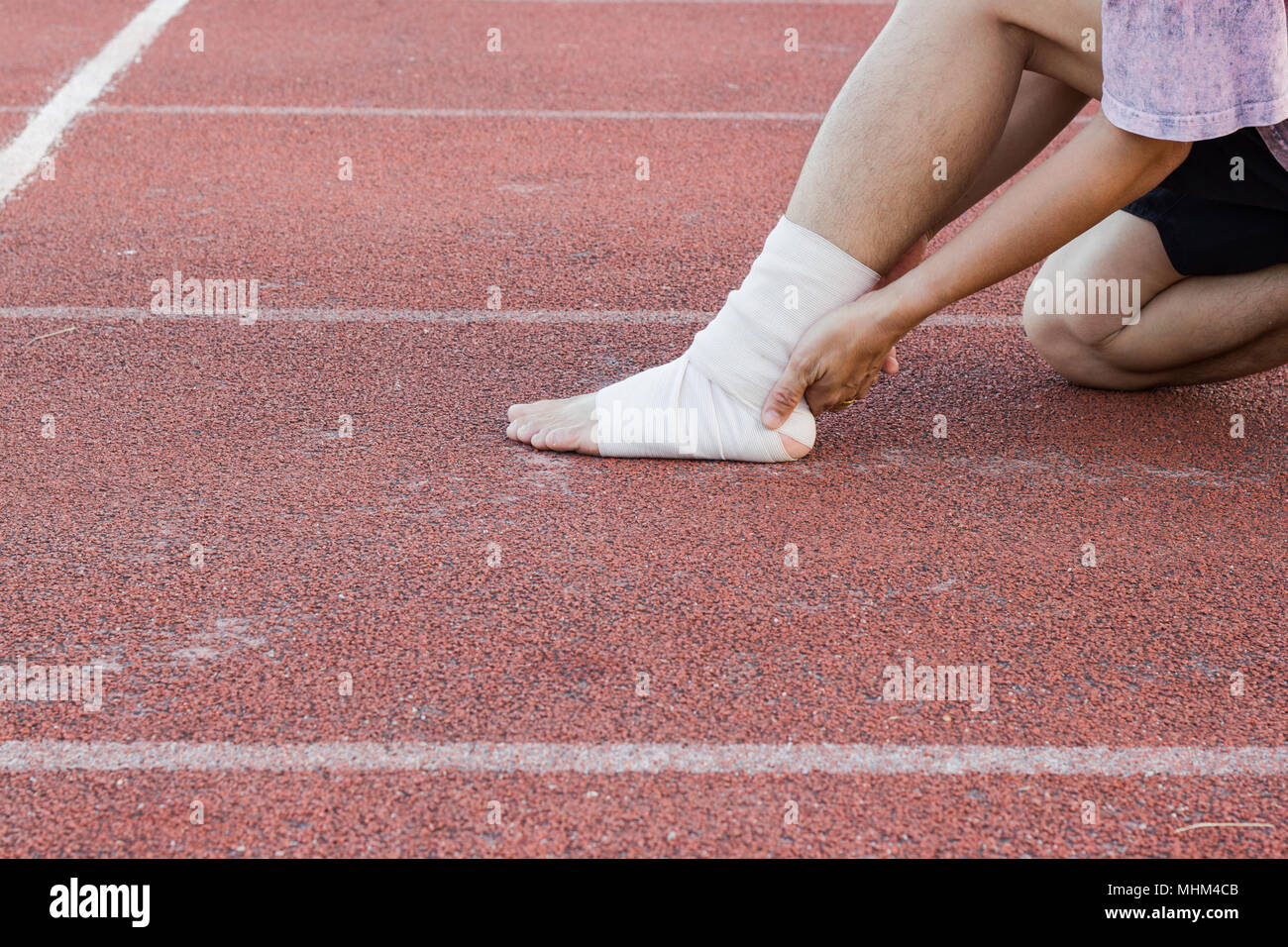 Male athlete applying compression bandage onto ankle injury of a