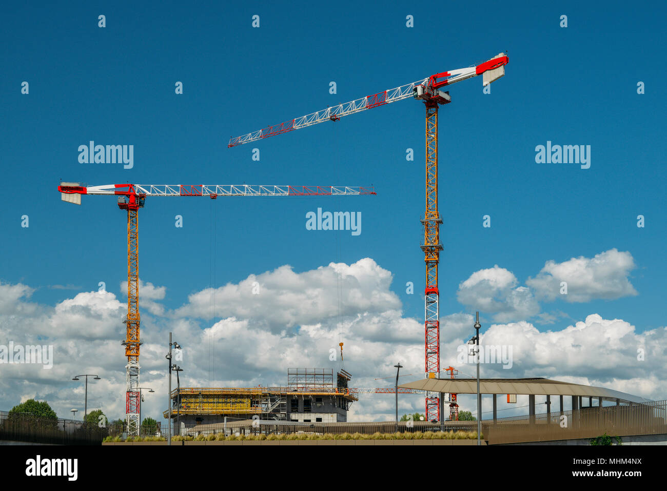 Construction cranes and unidentifiable construction workers at a building site with blue sky and copy space. Stock Photo