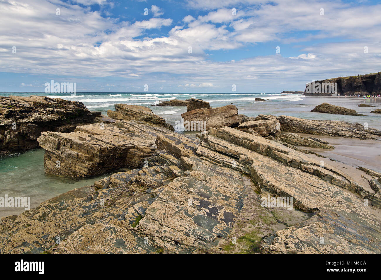 Strip of big stones on the sandy beach during an outflow. Black and gray stones, yellow sand and water of the ocean in the distance. Sunny summer day Stock Photo