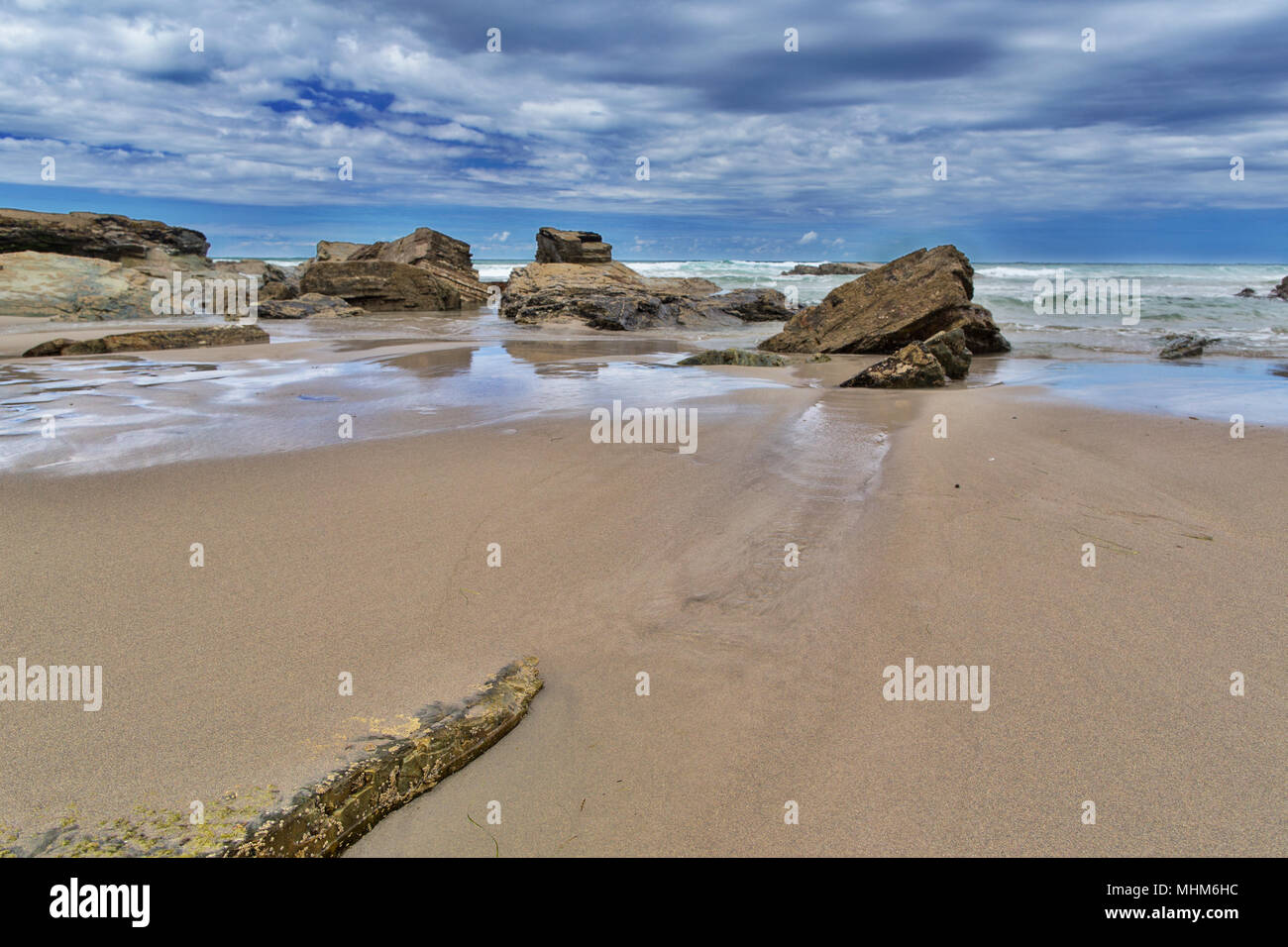 Strip of big stones on the sandy beach during an outflow. Black and gray stones, yellow sand and water of the ocean in the distance. Sunny summer day Stock Photo