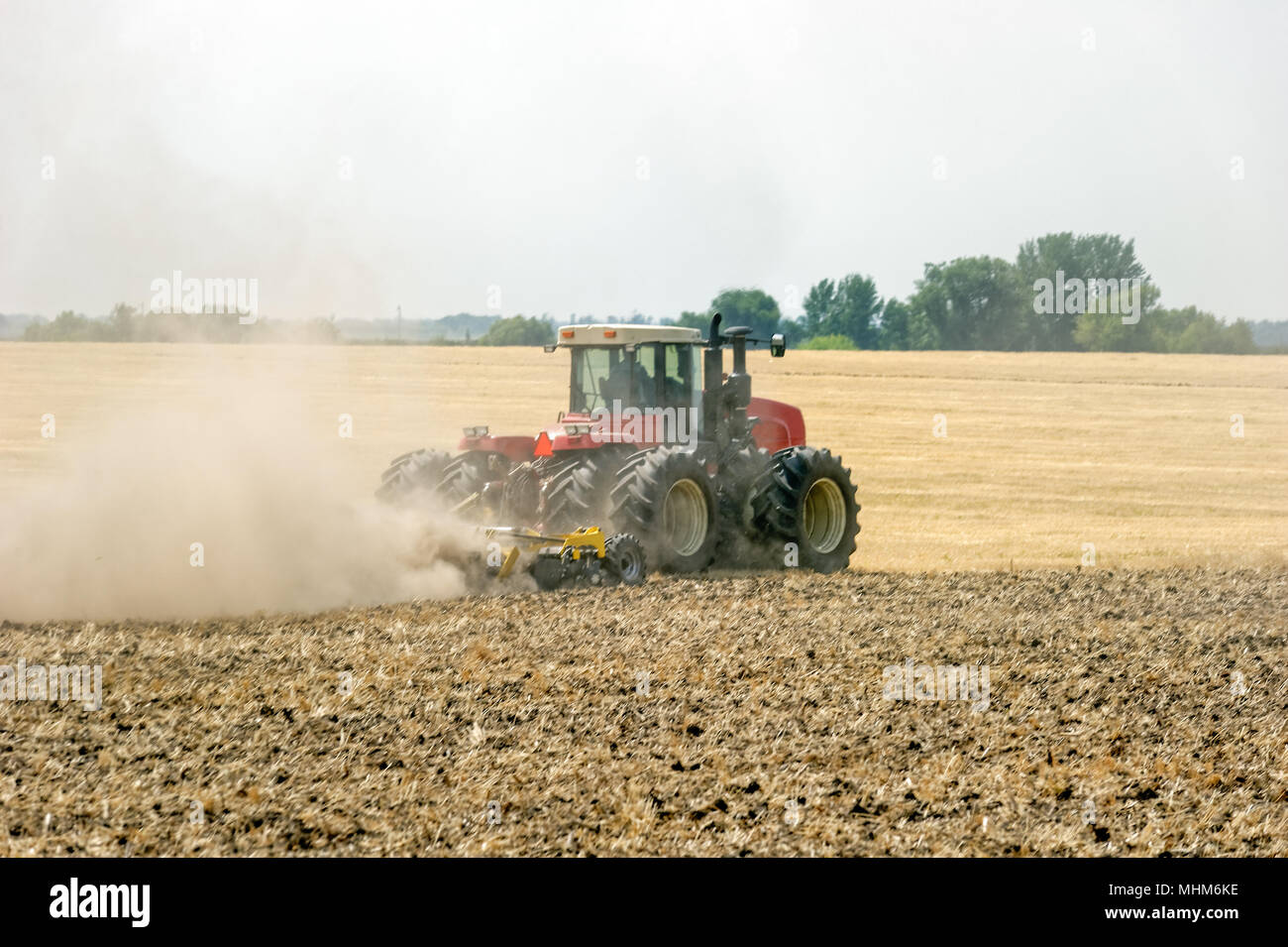 Tractor preparing land with plow, sunny summer day at agricultural field Stock Photo