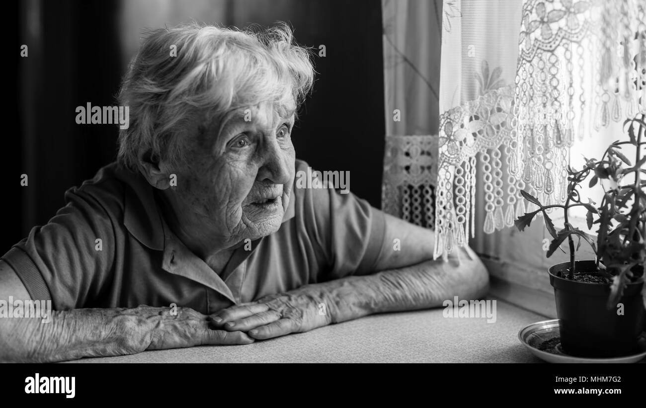 An elderly woman looks sadly out the window. Stock Photo