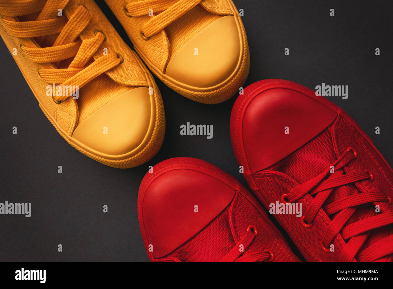 Young adult people on a love date, conceptual image. Top view of two pair of casual sneakers, yellow and red, from above close to each other Stock Photo