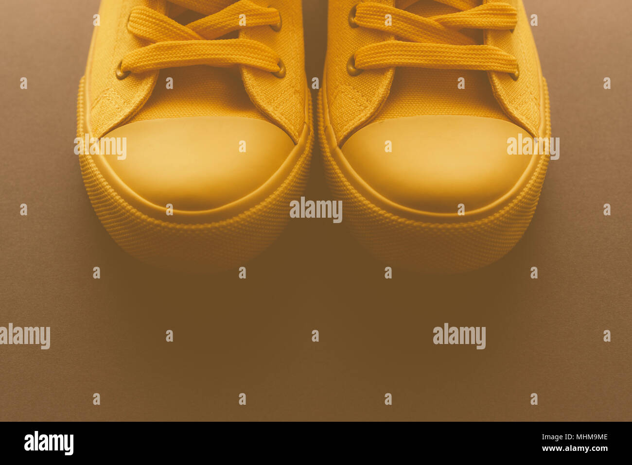 Brand new yellow sneakers on the floor, retro toned youth lifestyle footwear concept with copy space Stock Photo