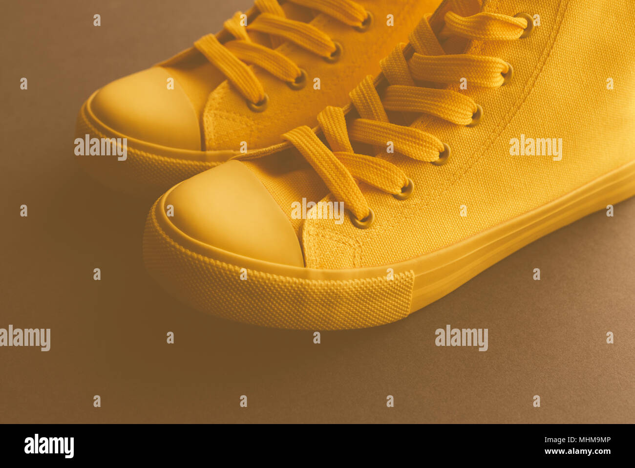Brand new yellow sneakers on the floor, retro toned youth lifestyle footwear concept with copy space Stock Photo