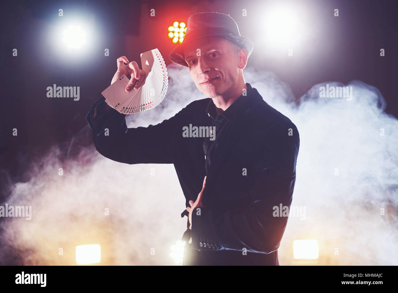 Magician showing trick with playing cards. Magic or dexterity, circus, gambling. Prestidigitator in dark room with fog Stock Photo