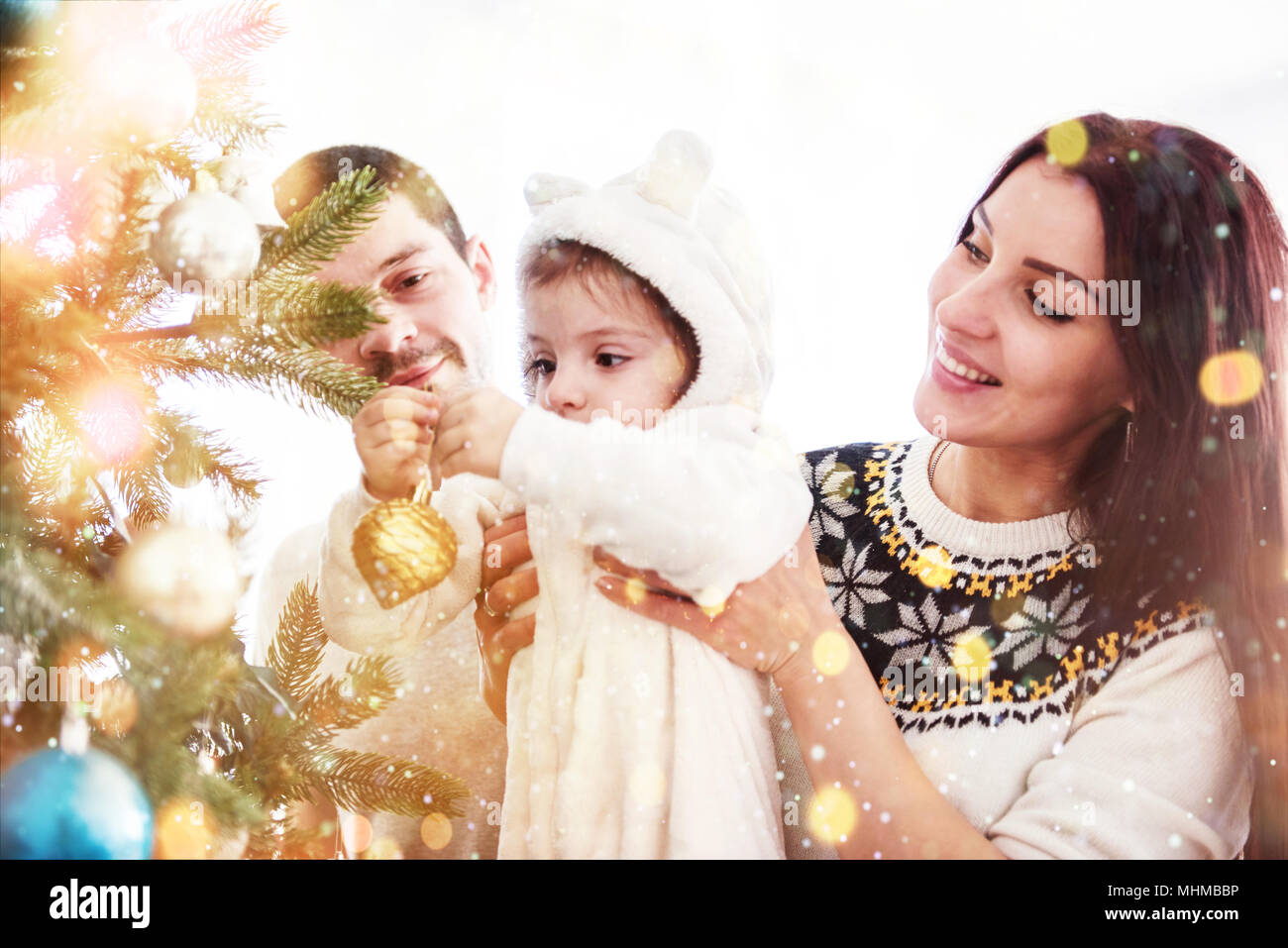 Happy Family Decorating Christmas Tree together. Father, Mother And Daughter. Cute Child Stock Photo