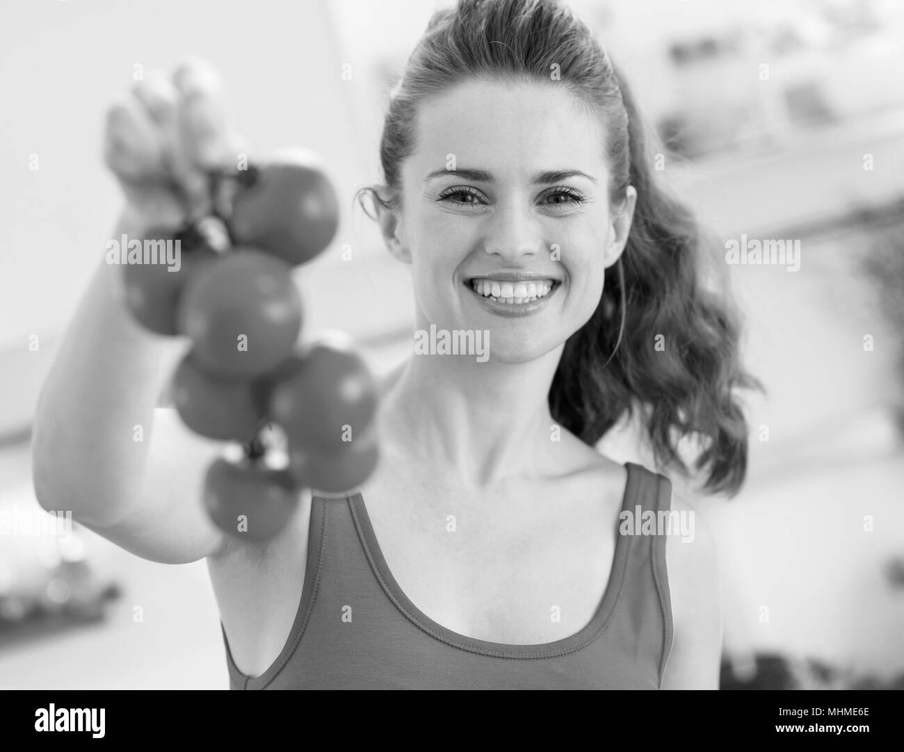 Happy young woman holding bunch of tomato in kitchen Stock Photo