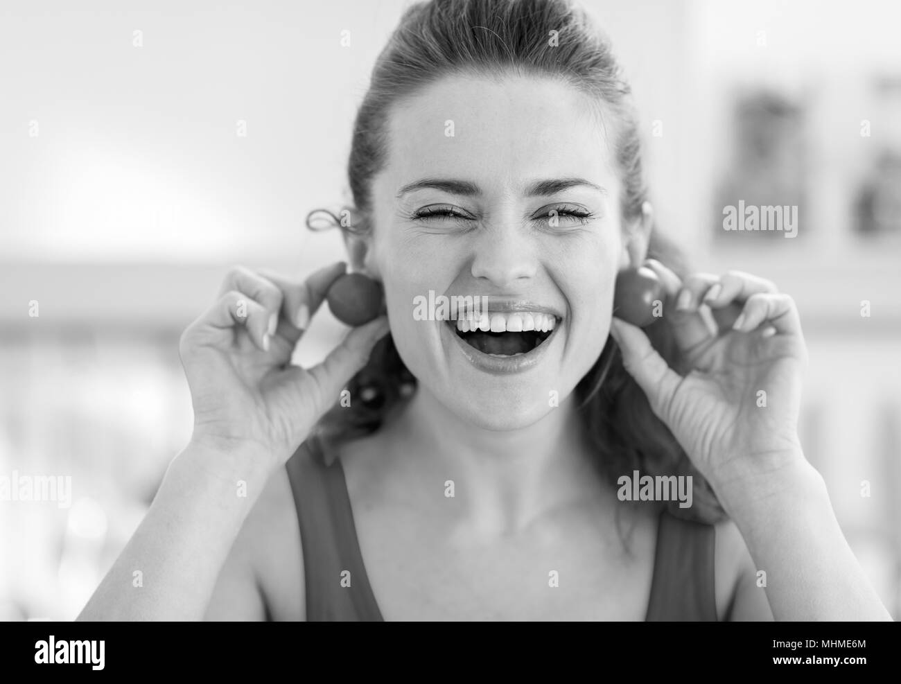 Smiling young woman using cherry tomato as earrings Stock Photo