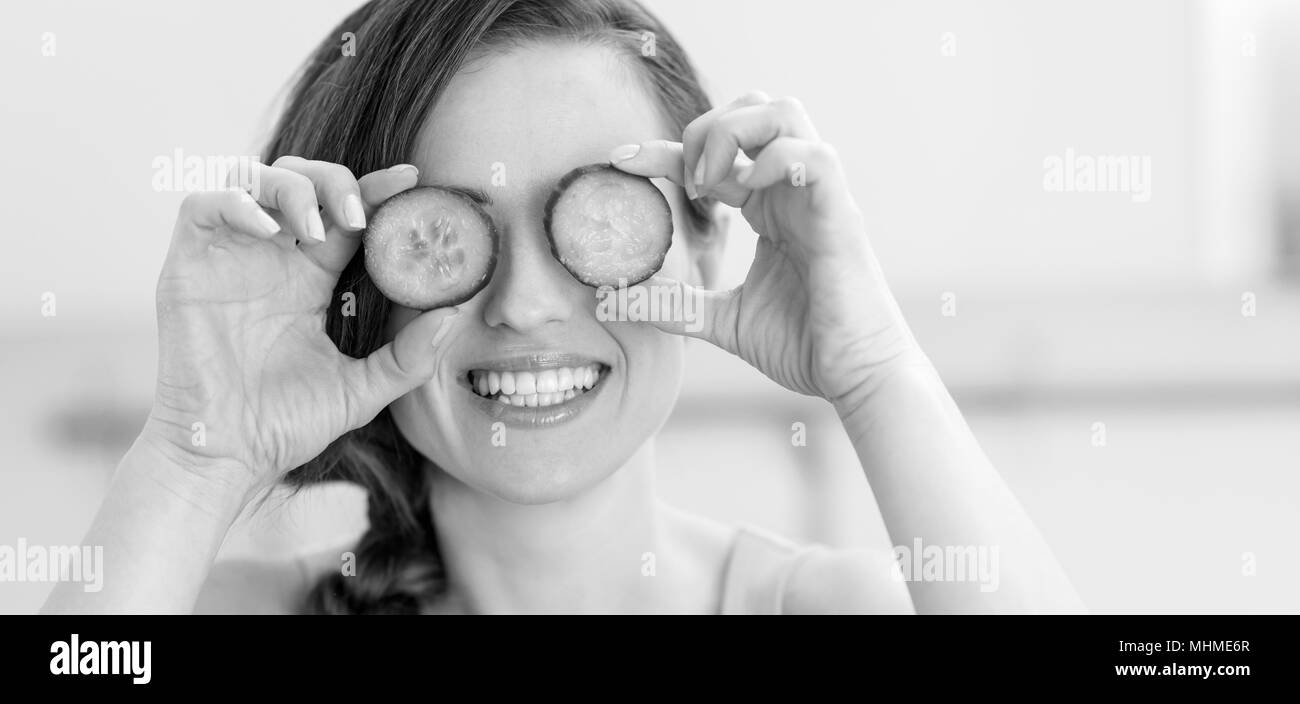 Smiling young woman holding slices of cucumber in front of eyes Stock Photo