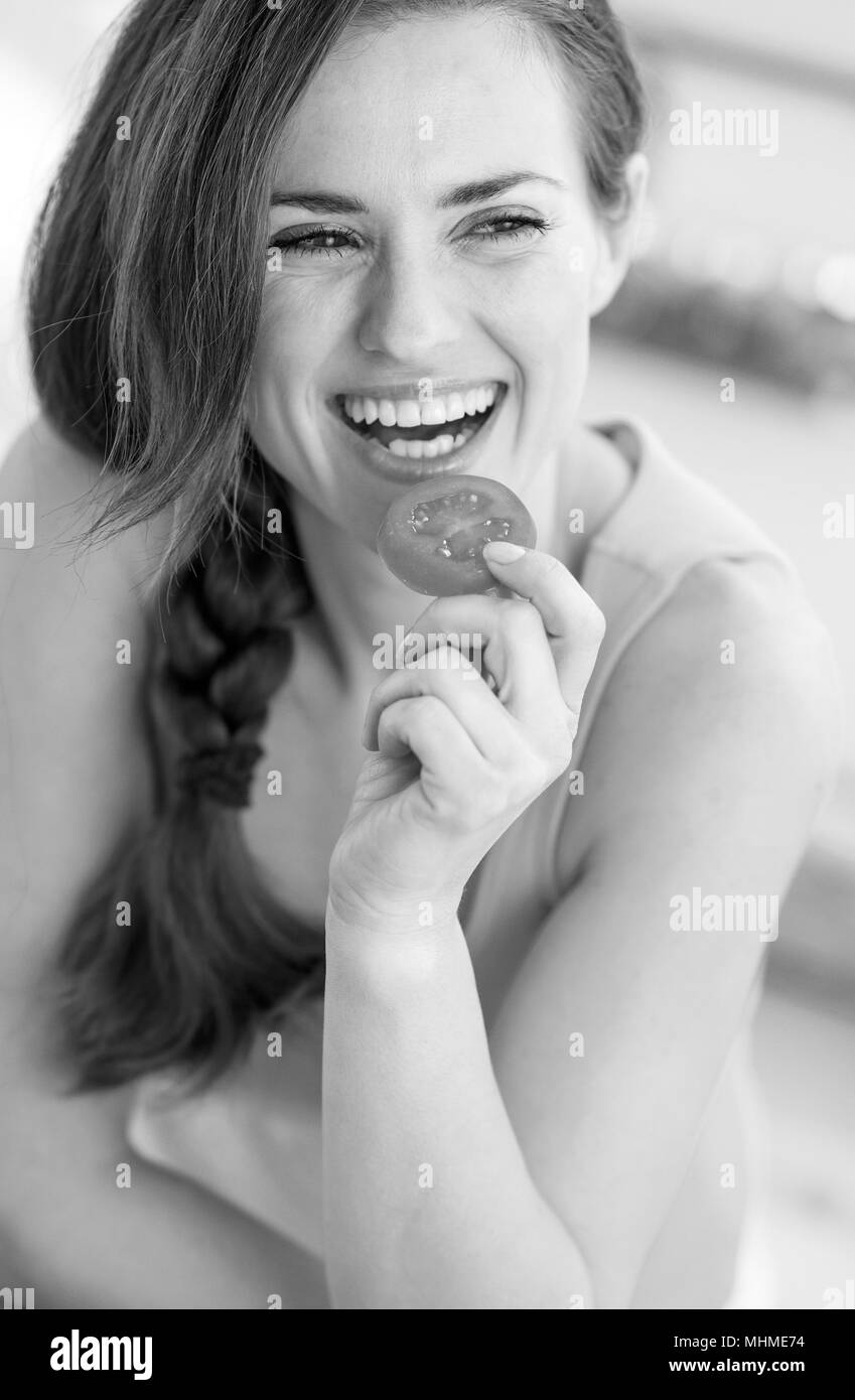 Smiling young woman eating tomato Stock Photo