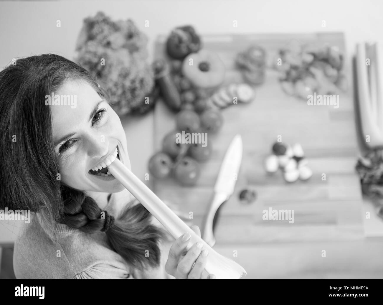 Happy young woman eating celery in modern kitchen Stock Photo