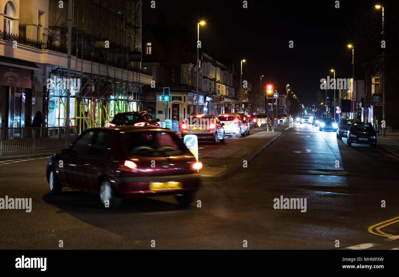 Cars on a road in a British town at night with lights on in England, UK. Stock Photo