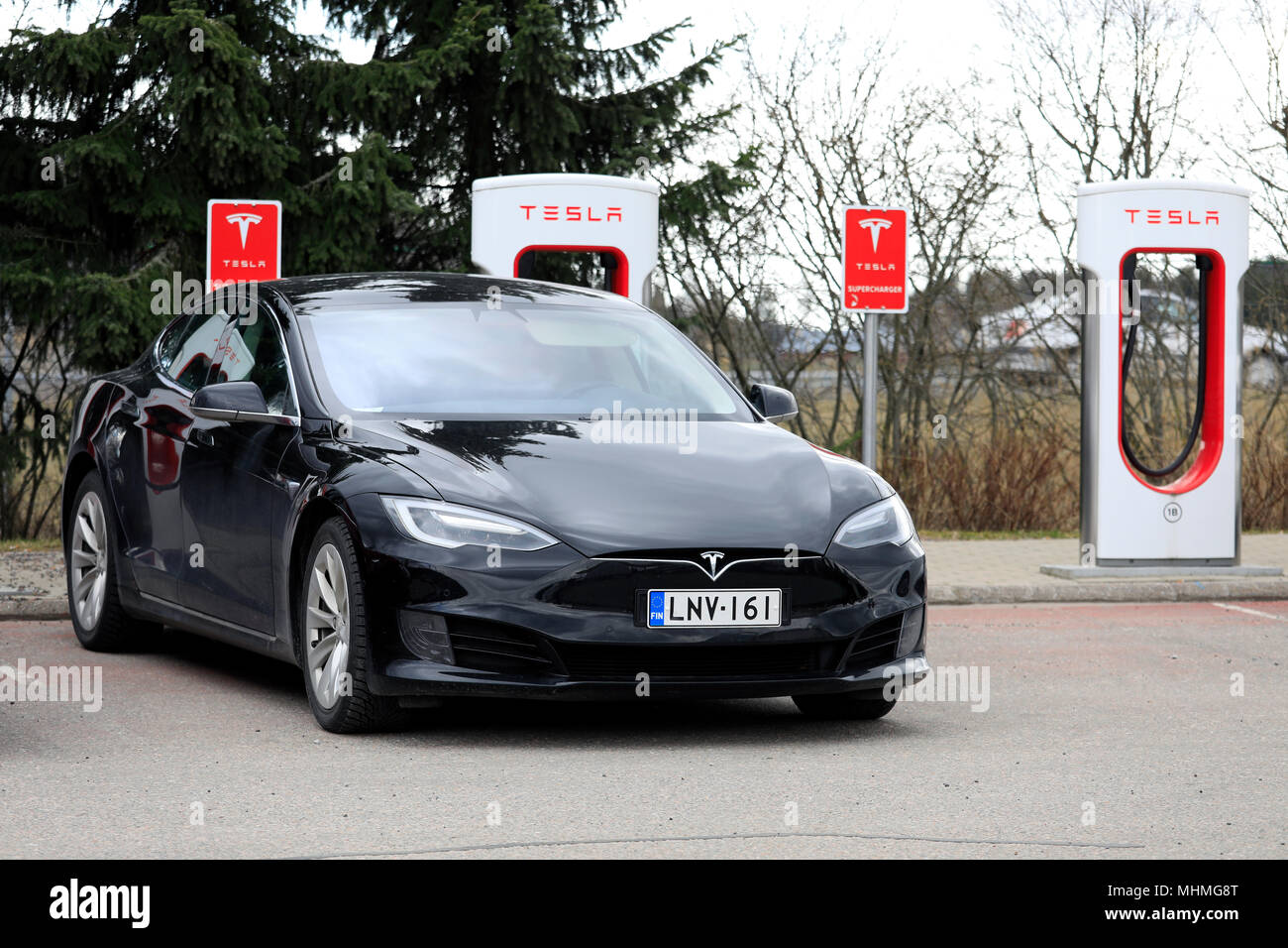 Black Tesla Model S electric car of the updated or facelift exterior design is charging battery at Supercharger station on a day of spring in Paimio,  Stock Photo