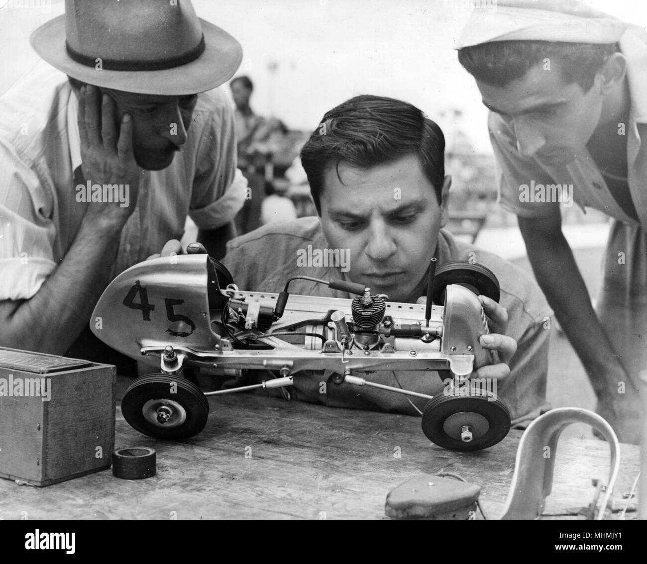 Three men examine a model racing car before the start of the big race       Date: 1950s Stock Photo