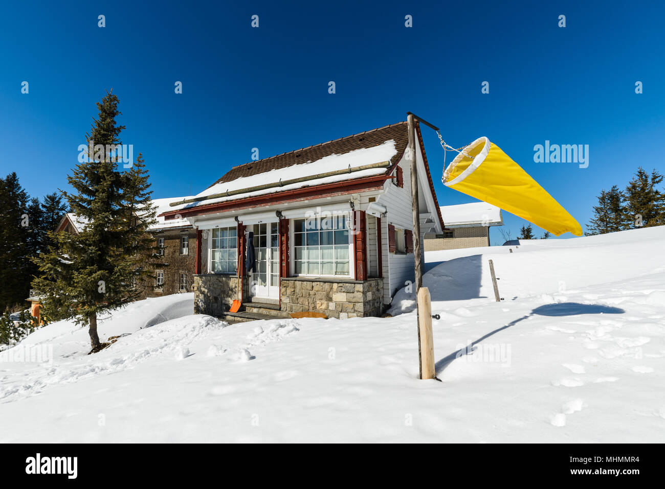 A small little tiny house cabin hut shack on Kulmweg at Rigi mountain Kulm with huge large big bright yellow windsock on a clear spring day Stock Photo