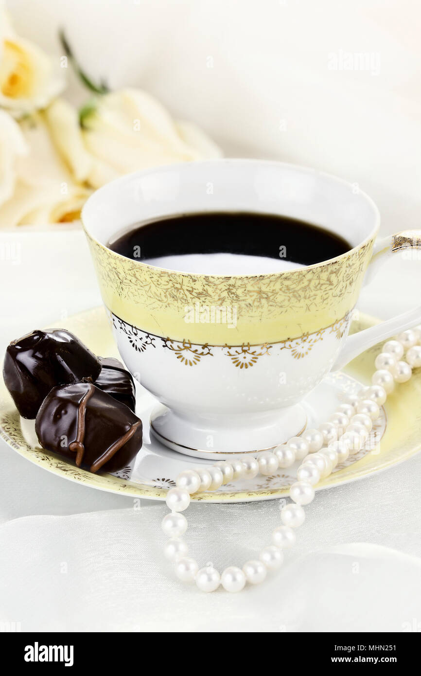 Close up of a cup of coffee chocolate candies and pearl necklace. Roses in the background. Shallow depth of field. Stock Photo