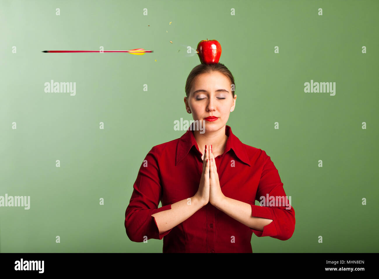 Woman meditating with an apple on her head, shot through by an arrow Stock Photo