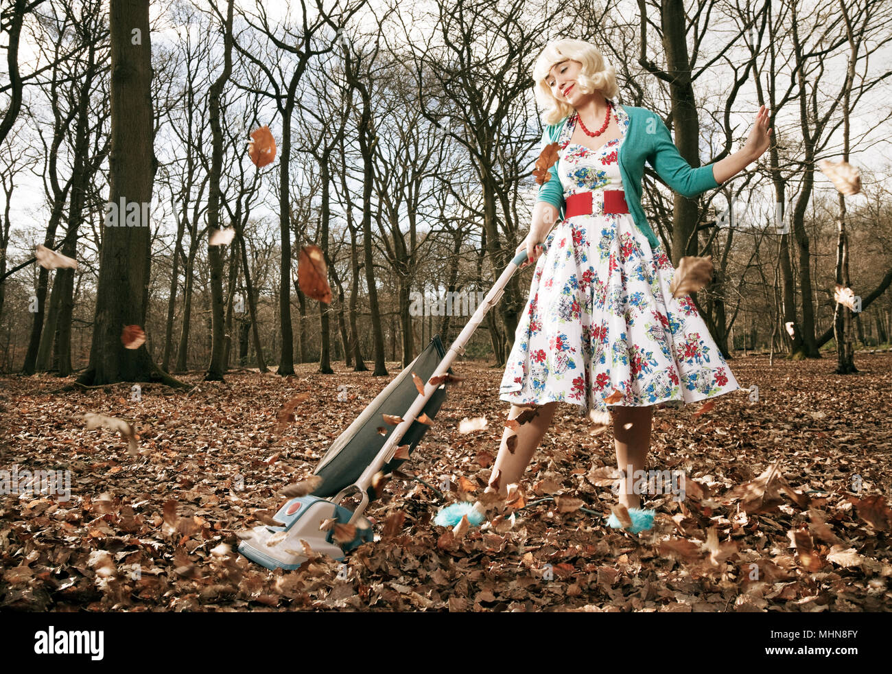 Woman in retro style vacuuming up leaves in the woods Stock Photo