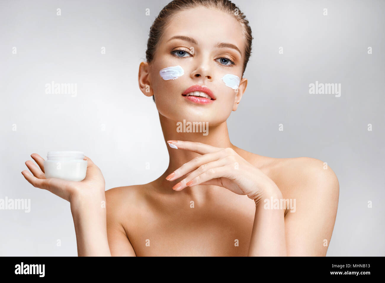Beautiful young girl with cosmetic cream on her face. Photo of woman with flawless skin on grey background. Skin care and beauty Stock Photo