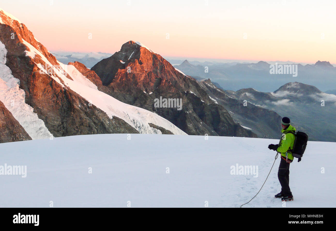 a male mountain climber stands on a high alpine glacier at dawn and admires the fantastic view ouf the surrounding landscape Stock Photo