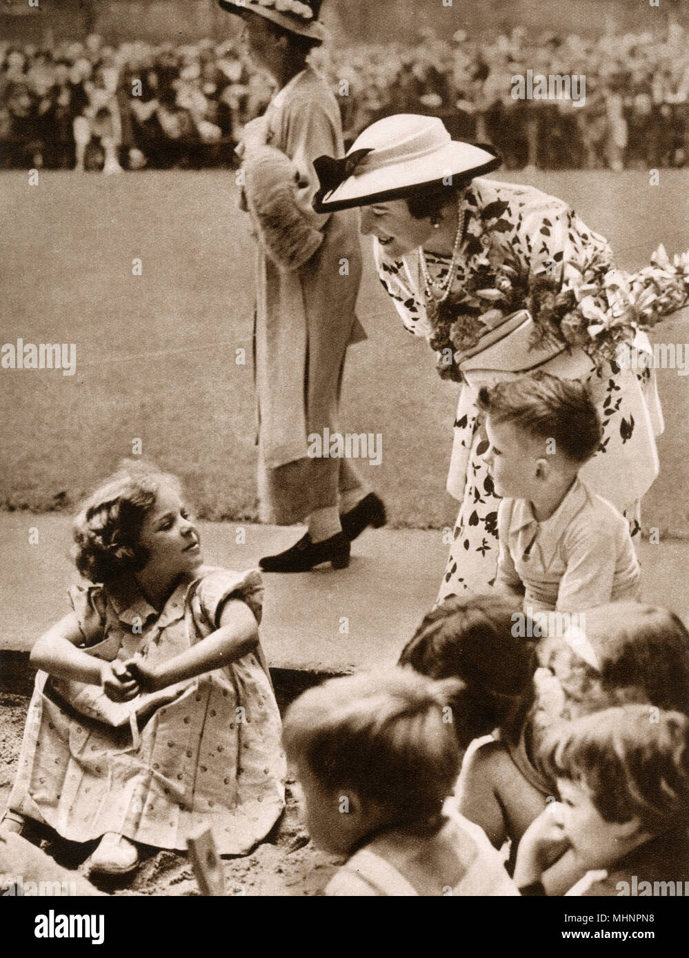 On first day of the court moving from full to half-mourning, Elizabeth, Duchess of York (later the Queen Mother 1900-2002), opens Corams Field and Harmsworth Memorial Playground, saving the old Foundling Hospital site as playgrounds for the children. The Duchess is here talking to children playing in the sandpit.     Date: 1936 Stock Photo